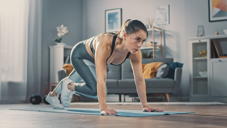 Frau beim intensiven Ganzkörpertraining im Wohnzimmer, fokussiert auf ihre Fitnessübungen auf einer Yogamatte.